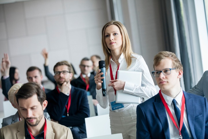 Confident businesswoman holding microphone while asking questions during seminar